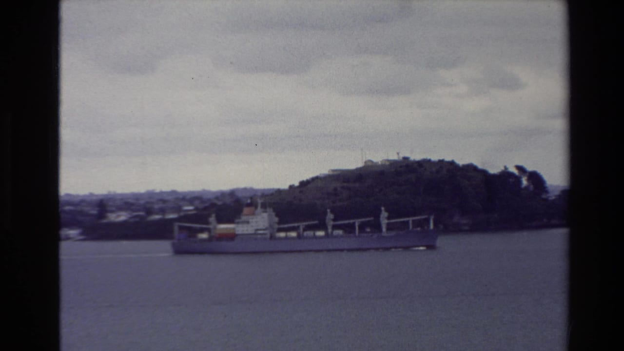 1981 New Zealand 8mm frame showing a cargo ship on harbor water with a wooded hill and overcast sky behind it.
