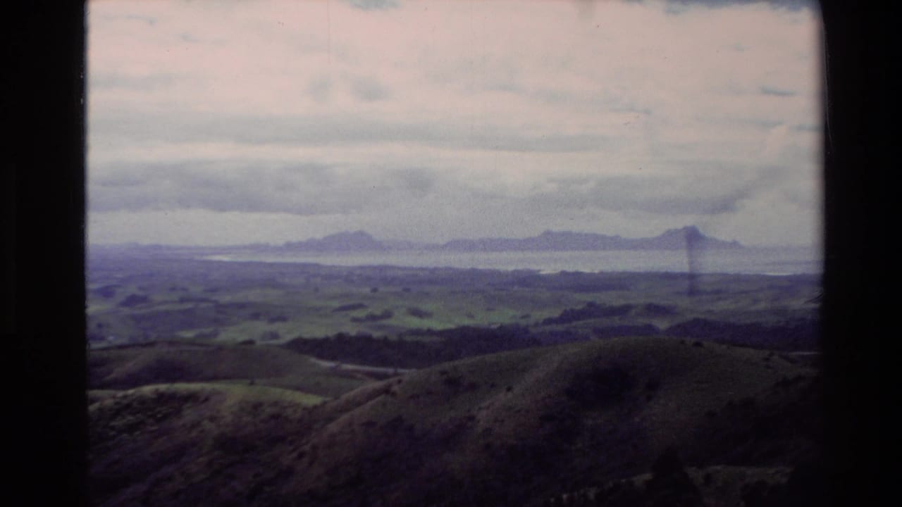 1981 New Zealand 8mm frame showing rolling green hills and distant mountains beneath a cloudy sky.