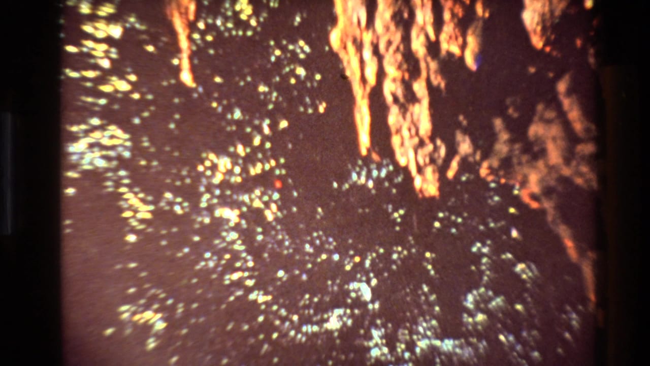1981 New Zealand 8mm frame showing a dark mine-like surface with flickering yellow-green light specks and orange illuminated rock texture.