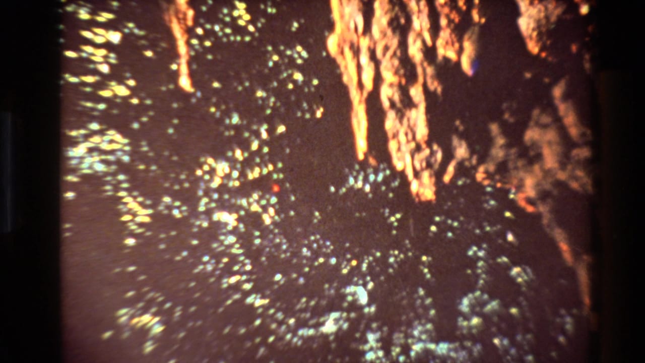 1981 New Zealand 8mm frame with scattered light flecks across a dark mine-like surface and orange illuminated rock forms at the top and right.