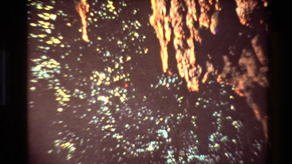 1981 New Zealand 8mm frame showing blurred bright flecks and orange rock-like texture in a dark industrial coal-mine setting.