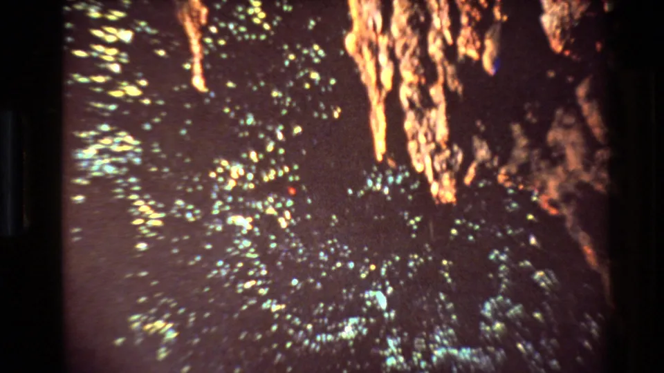 1981 New Zealand 8mm frame with dense yellow-green specks, orange illuminated formations, and a dark mine-like background.