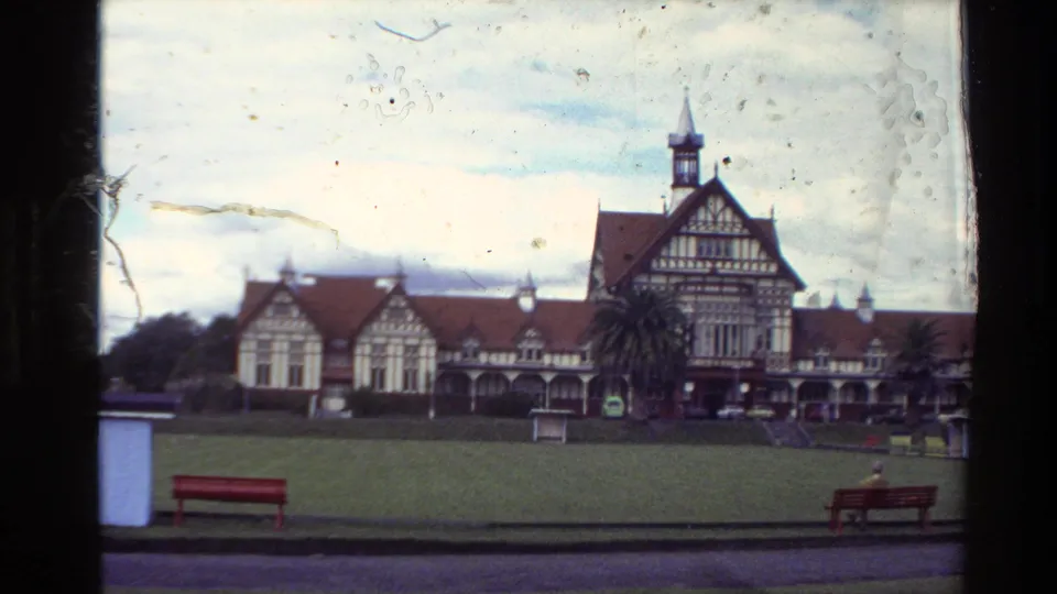 1981 New Zealand 8mm frame showing a wide lawn, benches, and a large Tudor-style building with red roofs and a central tower.