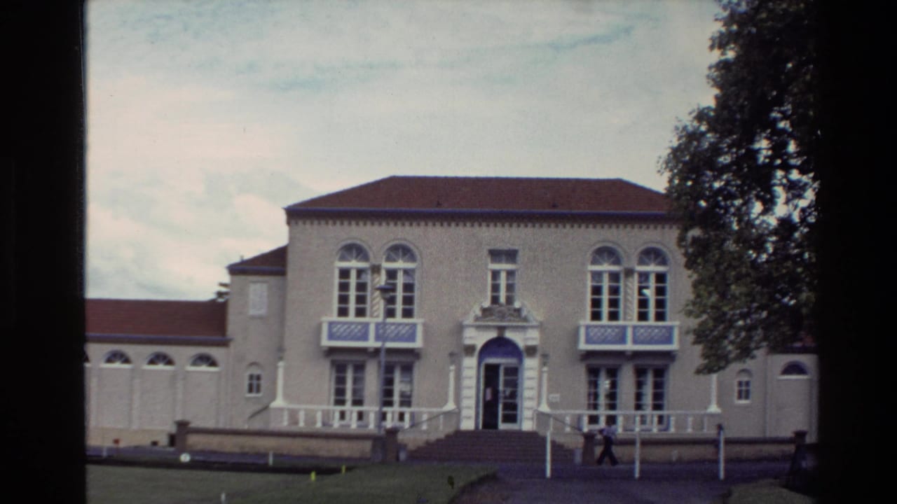 Tan building with blue-trimmed windows and a person near the entrance.