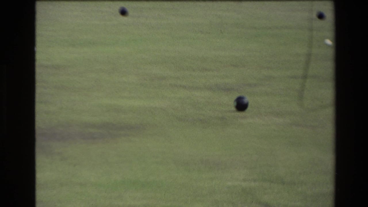 1981 New Zealand 8mm frame showing several dark bocce balls on a green lawn court with soft focus and film grain.
