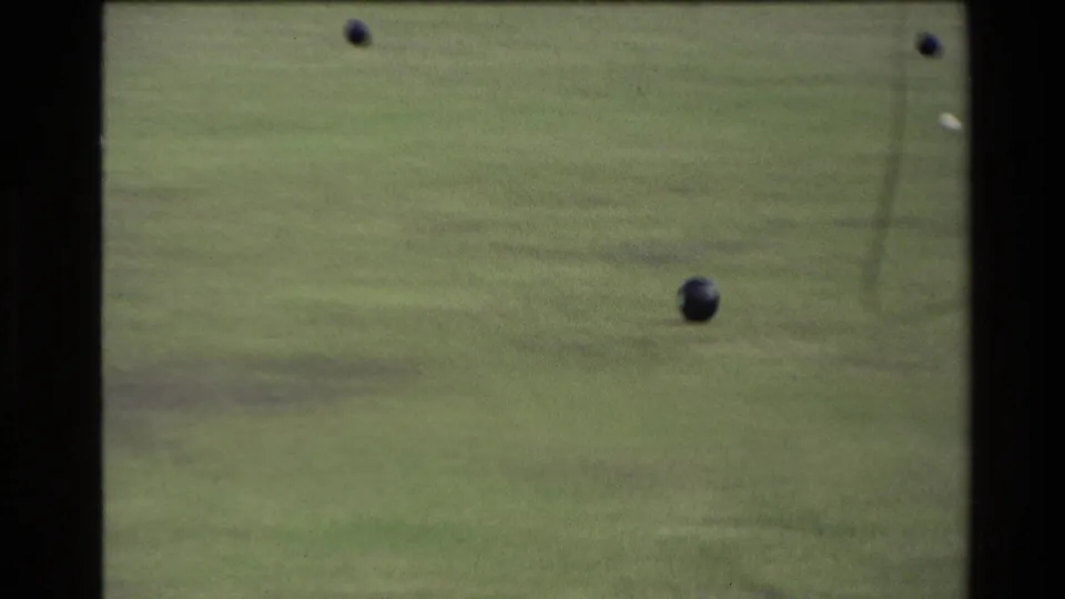 1981 New Zealand 8mm frame showing several dark bocce balls on a green lawn court with soft focus and film grain.