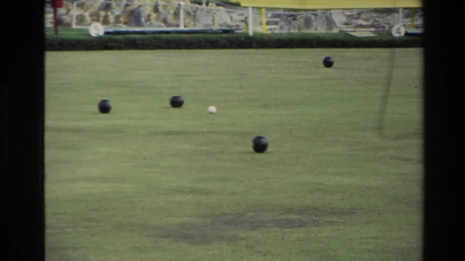 1981 New Zealand 8mm frame with bocce balls and a white pallino on a grass court, with stone edging and a yellow bench behind.
