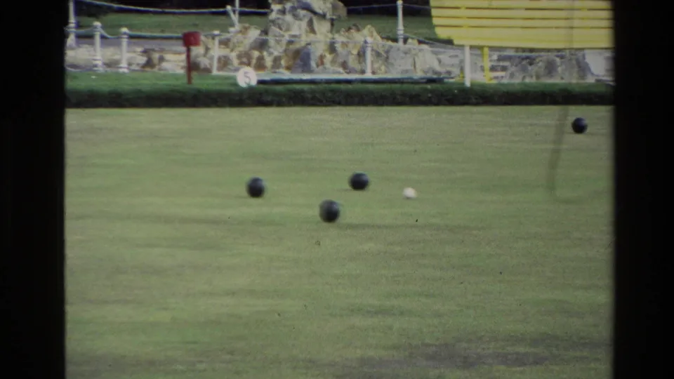 1981 New Zealand 8mm frame showing a small cluster of bocce balls and a white pallino on grass below a stone border and fence.