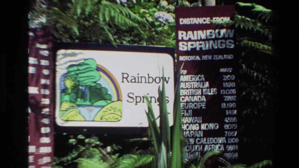 1981 New Zealand frame showing Rainbow Springs signage with a distance board and dense green foliage.