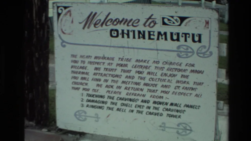 Closer 8mm view of the Ohinemutu welcome sign, with printed rules about respecting carvings and wall panels.