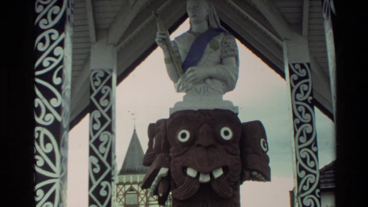 Carved face beneath a white statue, framed by patterned pavilion posts and roof beams.