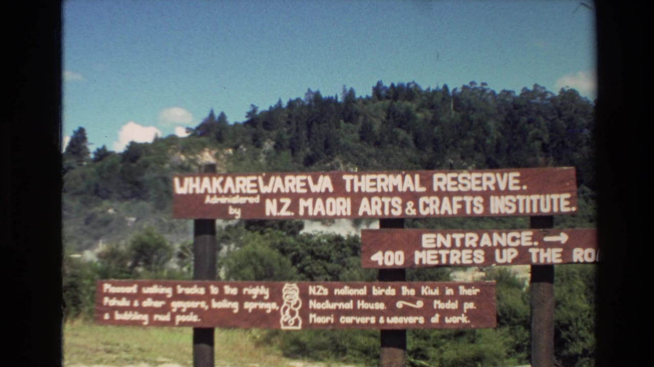 Wooden Whakarewarewa Thermal Reserve signs in front of forested hillside.