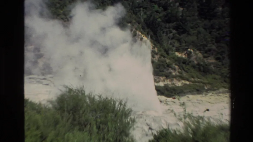 1981 New Zealand 8mm frame with a broad geothermal steam cloud spreading across shrubs and a dark wooded slope.