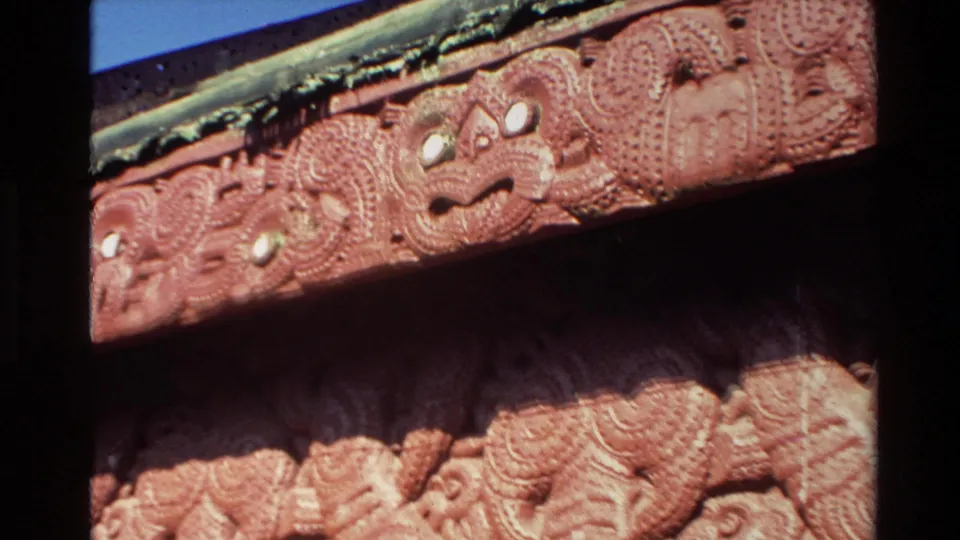 Angled close-up from the 1981 New Zealand clip showing red carved wall panels below a decorated roof edge.