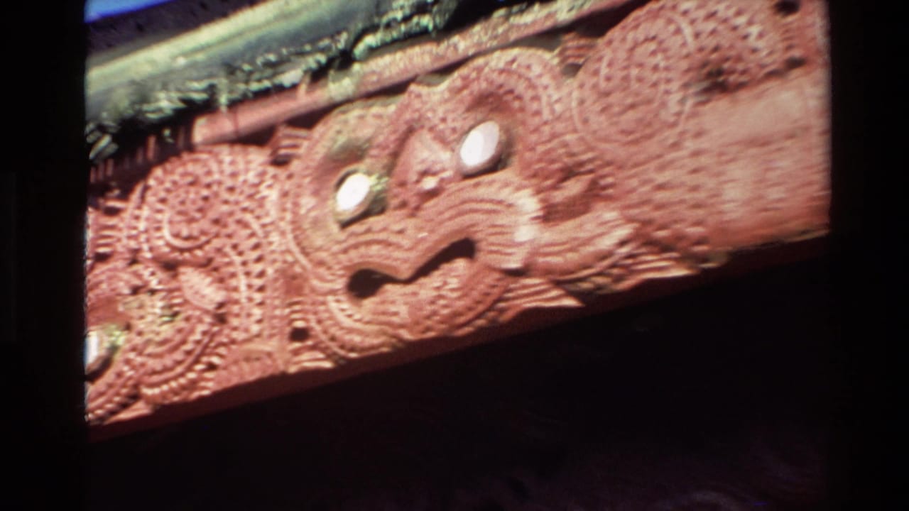 1981 New Zealand 8mm frame showing a close visitor view of red-brown carved Maori-style ornament with facial features and patterned surface detail.