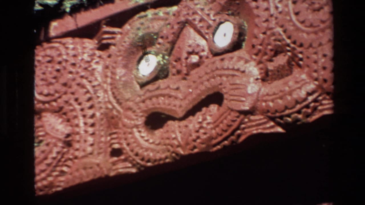 1981 New Zealand home-movie frame showing a carved face motif with bright eye details, dotted surface patterns, and dark surrounding exposure.