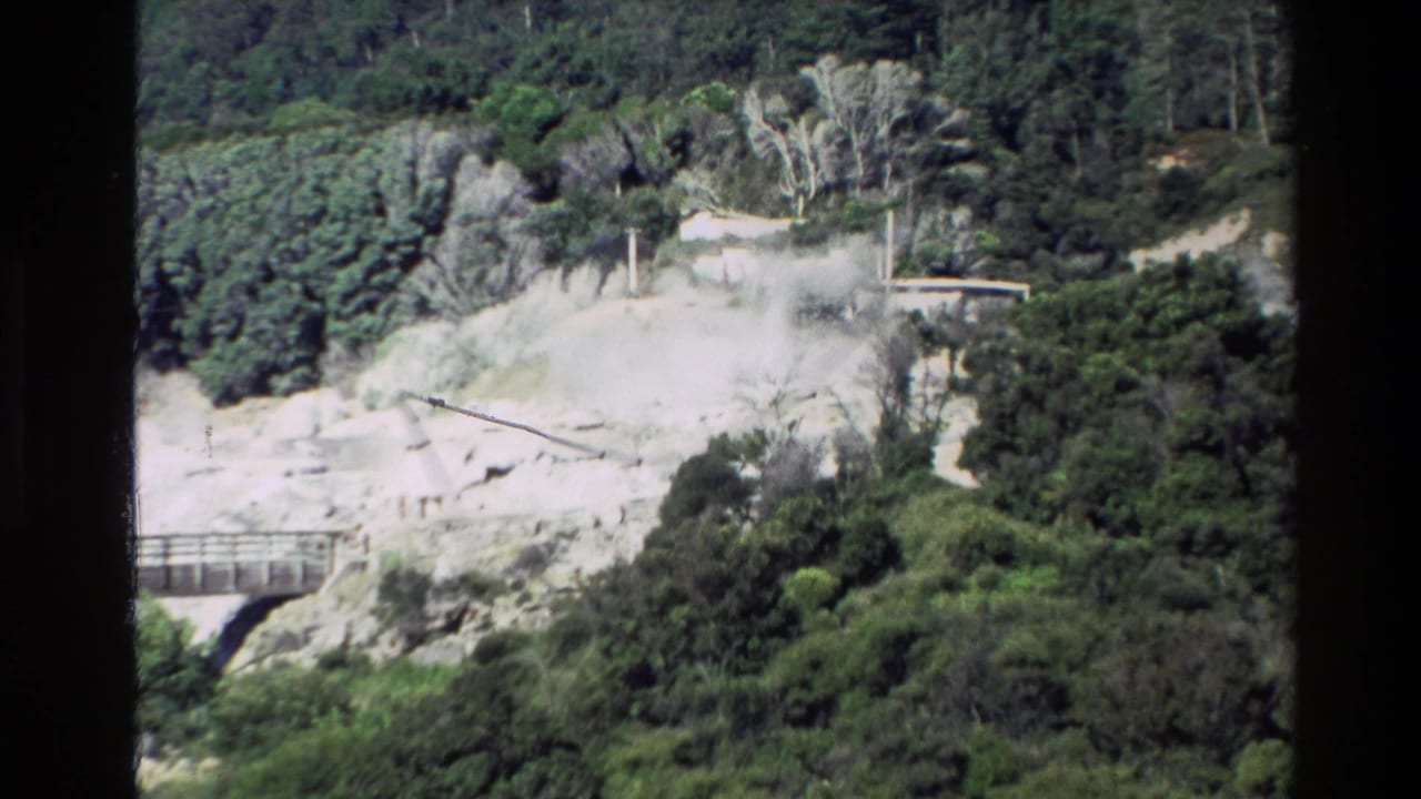Pale geothermal slope with vegetation, a walkway, and faint steam beginning to rise.