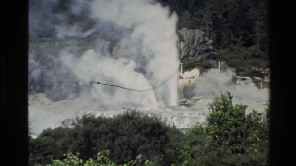 1981 New Zealand 8mm frame showing a geyser plume rising from pale geothermal terrain, with shrubs and dark film borders visible.