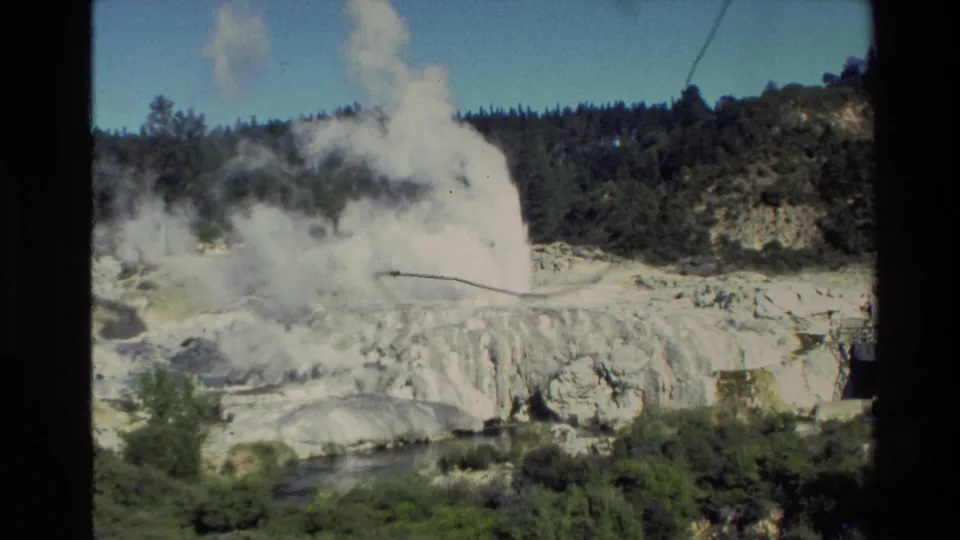 A wider 8mm view from New Zealand in 1981 shows a geyser plume above pale terraces, green vegetation, and a forested ridge.