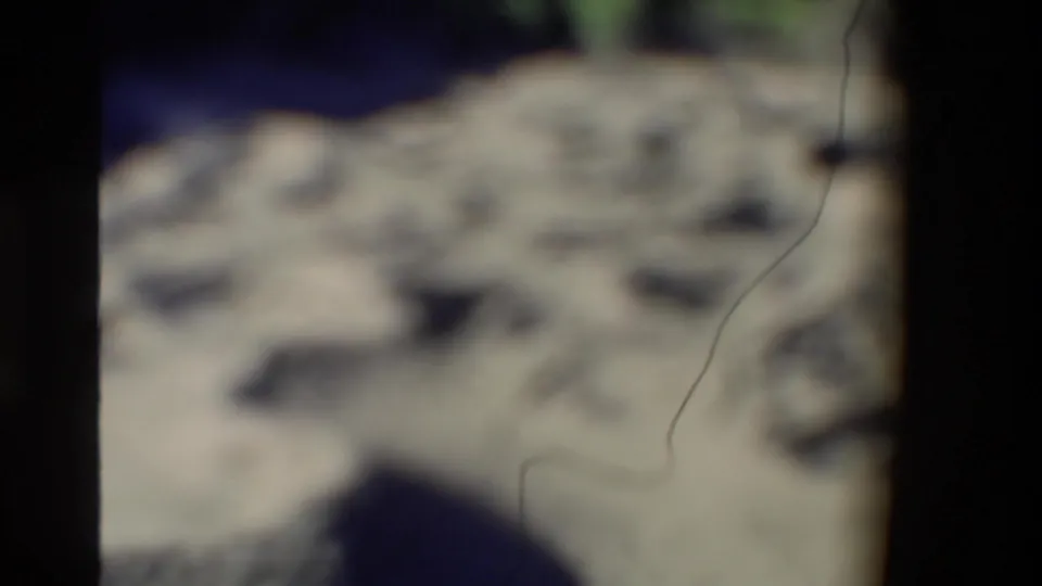 Soft-focused 8mm frame from the New Zealand geothermal sequence, showing pale mud-pot surface and dark wet areas in close view.