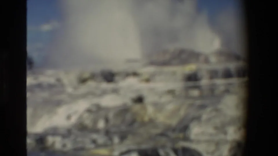 Soft-focused 1981 New Zealand 8mm frame showing steam over mineral terraces, with blurred foreground and visible dark film edge.