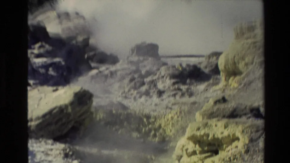 1981 New Zealand 8mm frame showing a steaming rocky geothermal pool, yellow-white deposits, and a faint rail-like line in the background.
