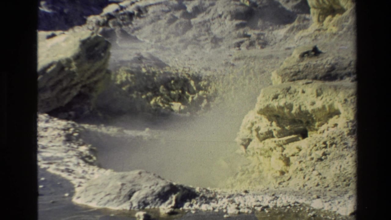 1981 New Zealand 8mm frame showing steam rising from mineral-stained geothermal ground and pale rock formations.