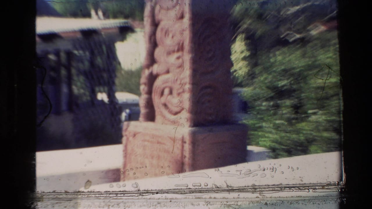 1981 New Zealand 8mm frame showing a carved brown monument near a light-colored church building and greenery.