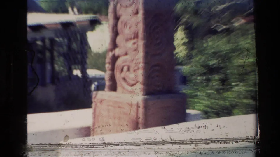 1981 New Zealand 8mm frame showing a carved brown monument near a light-colored church building and greenery.