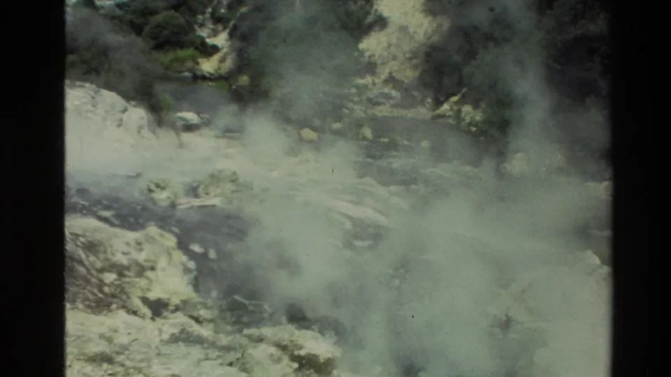 1981 New Zealand 8mm frame with geothermal steam obscuring parts of a rocky stream and wooded banks.
