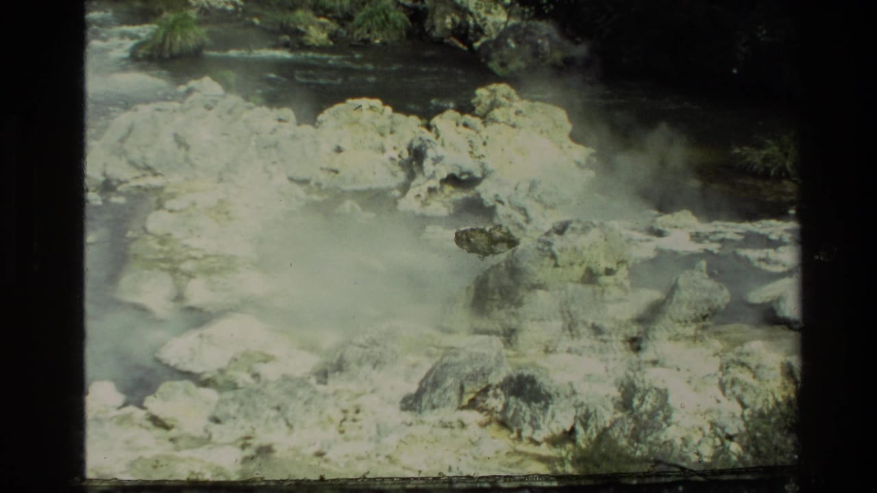 1981 New Zealand 8mm frame showing steam over rocky hot-spring water with trees and vegetation at the edge.