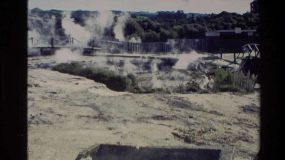 1981 New Zealand home-movie view of steam vents rising behind a wooden fence on pale geothermal ground.