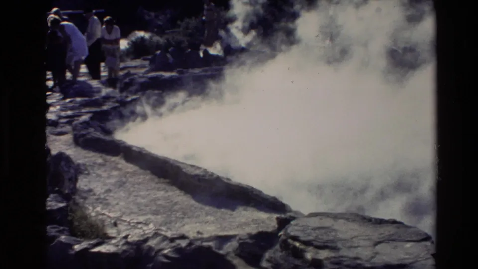 Tourists appear behind a heavy steam plume at a New Zealand geothermal site in 1981 8mm travel footage.