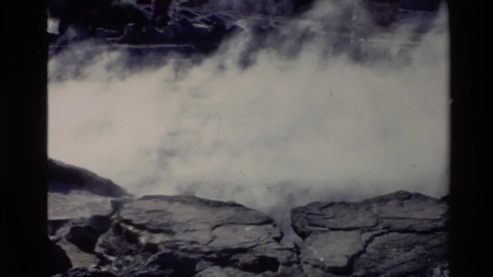 Dense white steam obscures part of a New Zealand geothermal spring, with dark rocks visible along the lower edge.