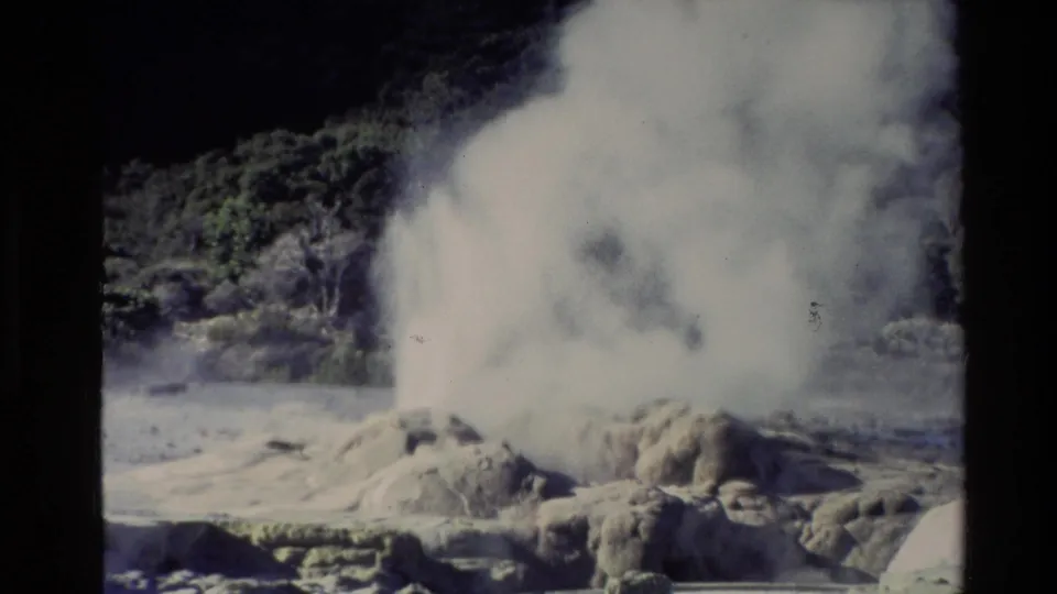 1981 New Zealand 8mm frame with a broad steam cloud spreading above a rocky geyser mound beside shallow geothermal water.