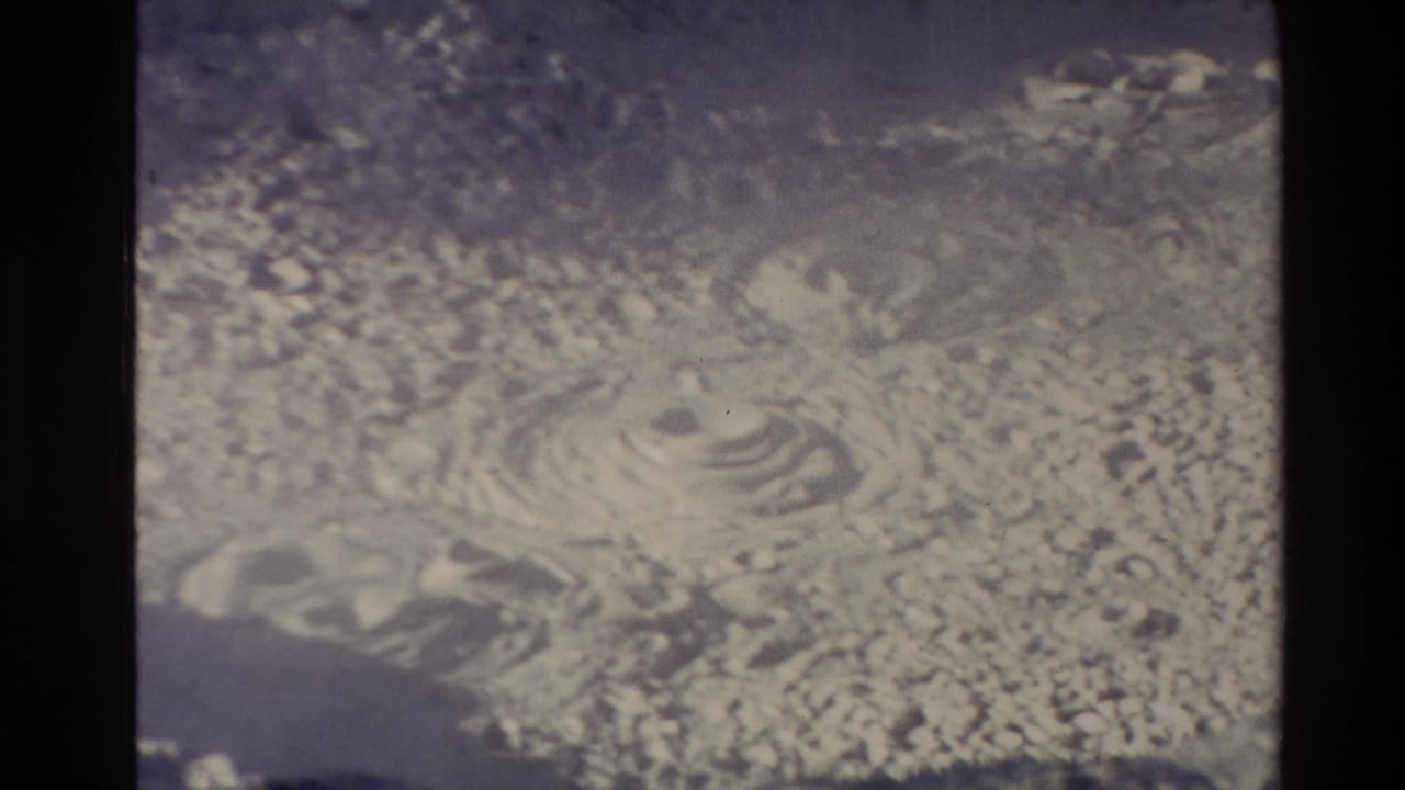 Mud pot surface with a central bubbling vent and rippled wet texture.