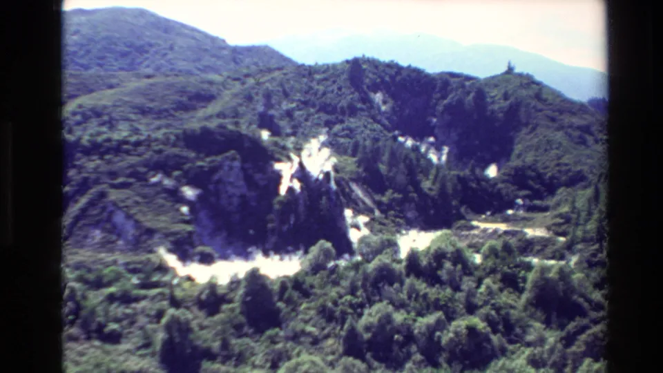 1981 New Zealand home-movie view of Waimangu's forested geothermal hills with pale steam and exposed light-toned ground.
