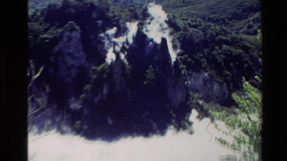 1981 New Zealand 8mm frame with overexposed steam rising around jagged volcanic rock and dense green hillside vegetation.