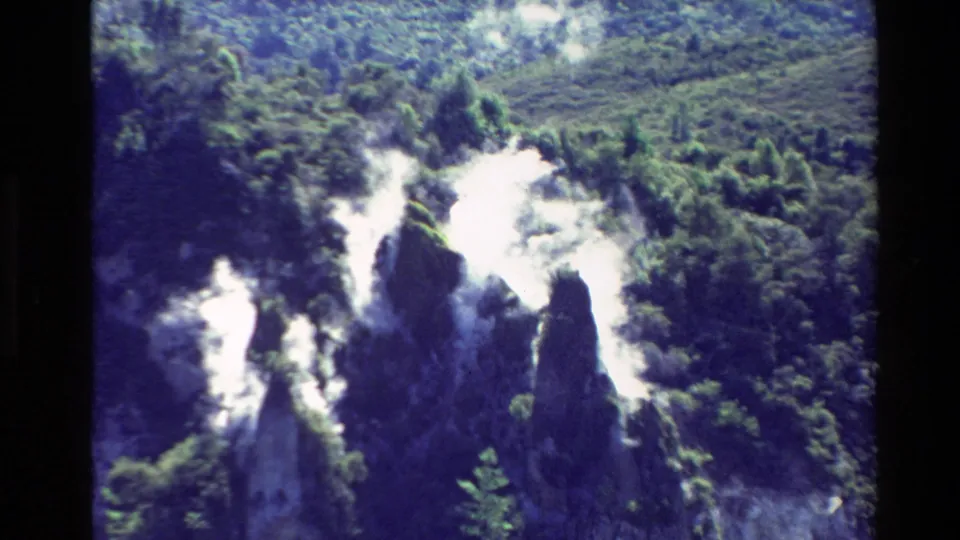 1981 New Zealand 8mm frame showing white volcanic steam drifting over forested slopes and dark rock formations.