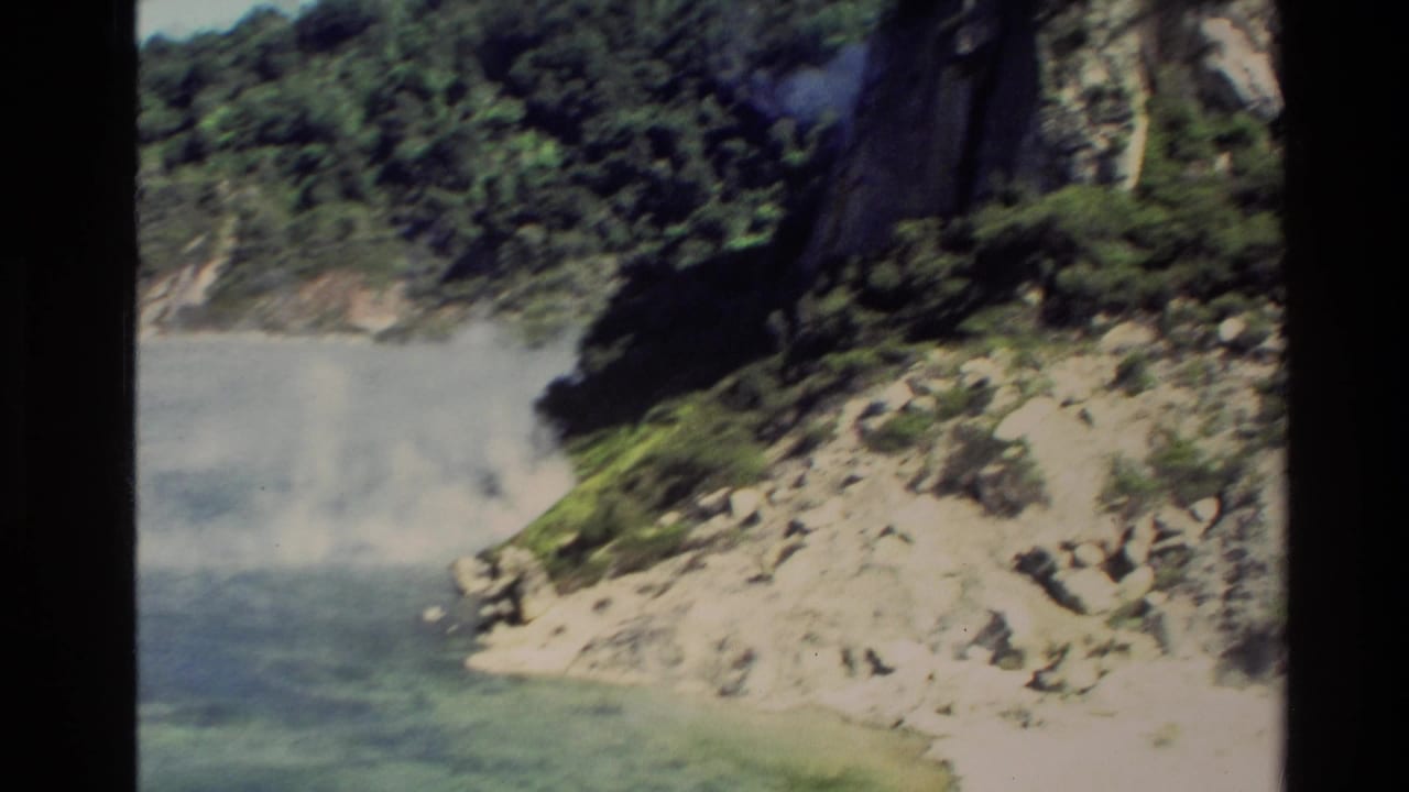 Steam rising beside rocky water below forested cliffs.