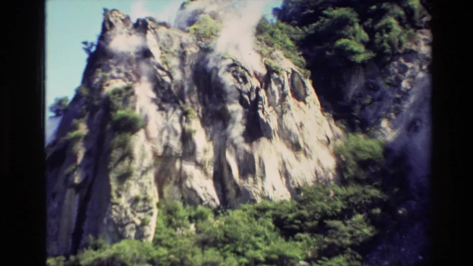1981 New Zealand 8mm frame showing a bright, rugged rock formation with shrubs and trees in a geothermal mountain setting.