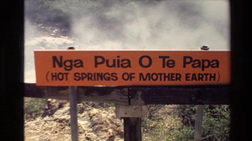Closer 8mm frame of the orange Nga Puia O Te Papa sign with steam drifting behind it in the New Zealand hot springs area.