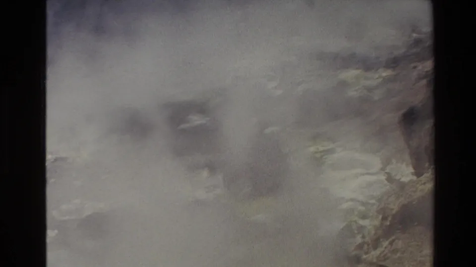 1981 New Zealand 8mm frame showing pale smoke or mist drifting over rugged mountain terrain with muted vegetation.
