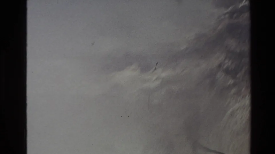 1981 New Zealand home-movie frame with a vapor-filled mountain view, dark film border, and barely visible rocky texture.