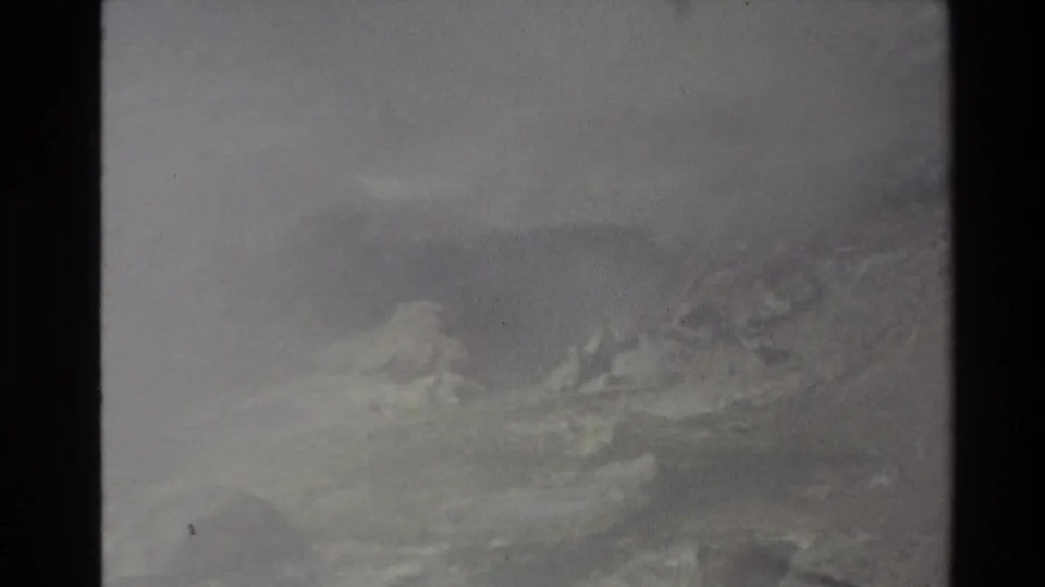 1981 New Zealand 8mm frame of smoky or misty mountain terrain, with pale vapor drifting across rocks and vegetation.