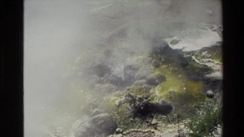 Steam rises from a rocky New Zealand geothermal area, with yellow-green mineral staining visible in the 8mm frame.