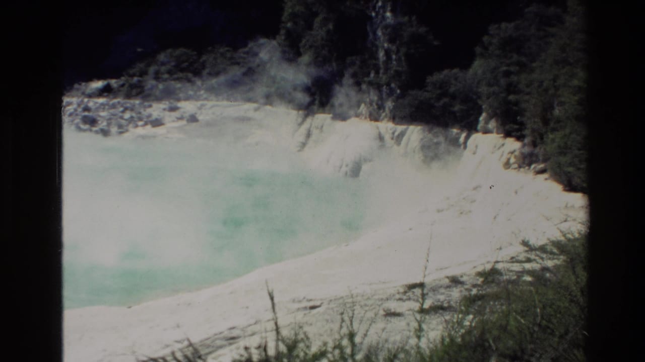 1981 New Zealand 8mm frame showing a turquoise hot spring beside pale mineral terraces and surrounding bush.
