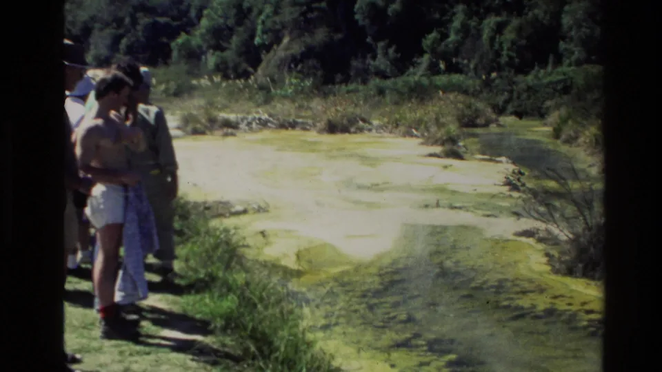 1981 New Zealand 8mm frame showing visitors beside a mineral-rich geothermal pool with green vegetation beyond.