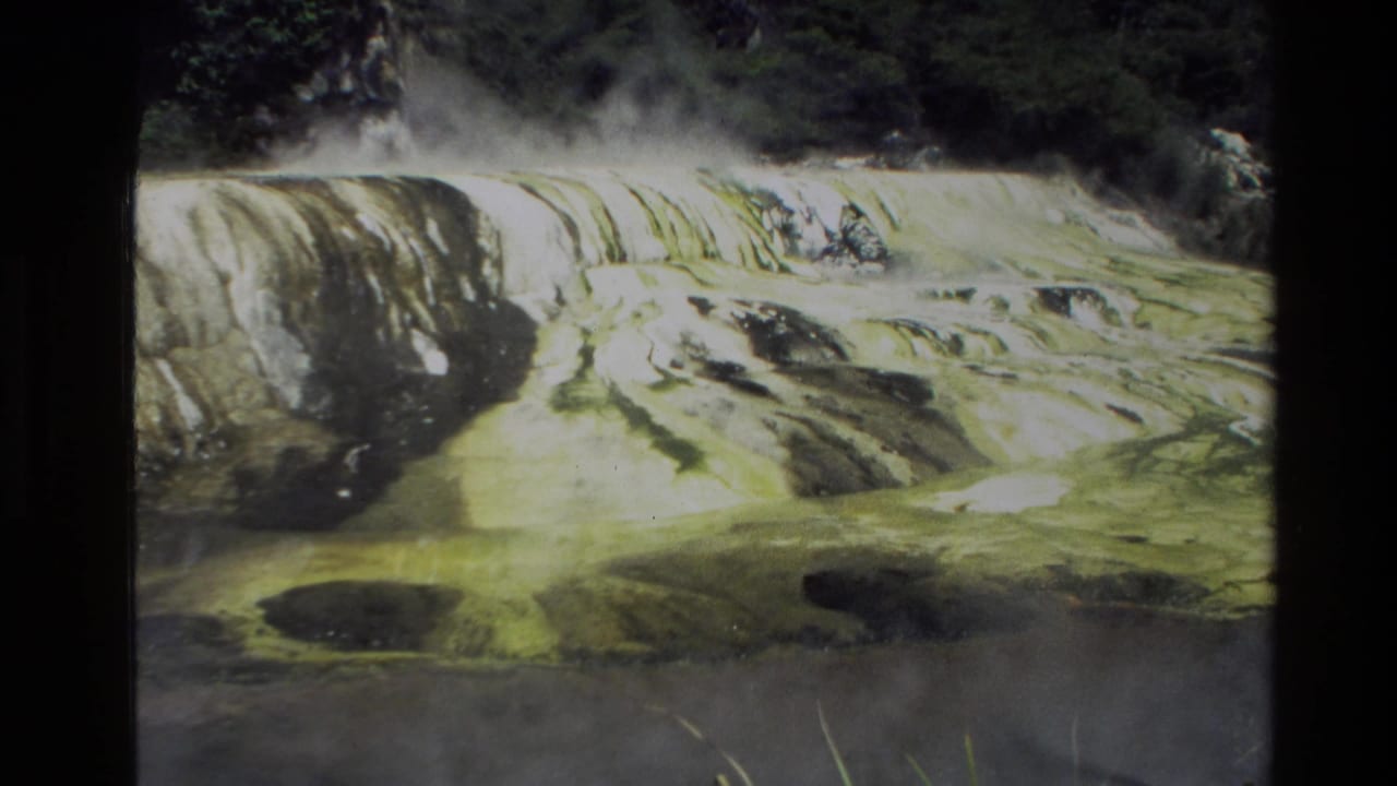 Steaming pale terraces or rock shelves with dark vegetation behind them.