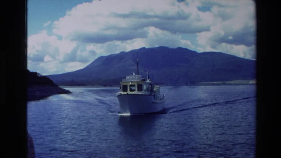 1981 New Zealand 8mm frame showing a small white motorboat on calm blue water with dark mountains and clouds in the distance.